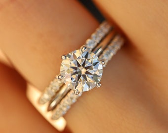 May include: A close-up of a hand wearing a three-piece diamond ring set. The center stone is a large, round brilliant diamond. The band is set with smaller diamonds.