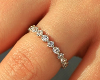 May include: A delicate eternity band ring with a row of small, round, clear gemstones set in a silver band.
