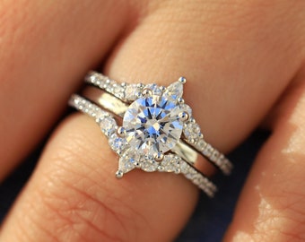 May include: A silver engagement ring featuring a large round centre stone and smaller stones set in a delicate, floral design. The ring is worn on a finger with a light skin tone.