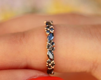 May include: A delicate gold band ring with a row of black marquise-shaped gemstones. The ring is set with small round black gemstones between the marquise stones.