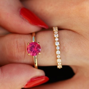 May include: A gold ring with a pink gemstone and a gold band with a row of small diamonds.
