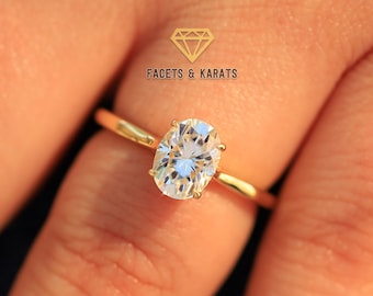 May include: A gold engagement ring with an oval-shaped diamond. The ring is on a person's finger.