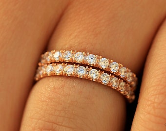 May include: Two delicate gold rings with a row of sparkling diamonds around each band. The rings are worn on a finger.