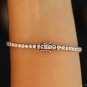 the image is showcasing the double safety clasp of a diamond tennis bracelet while being worn on the wrist. The brand name is Facets and Karats. The round cut diamonds are shining very beautifully.