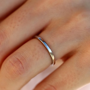 May include: A thin, silver band ring worn on a finger.