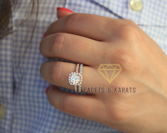 Puede incluir: Un anillo de compromiso de oro rosa con una piedra central redonda y un halo de piedras más pequeñas. La banda está acentuada con una fila de piedras más pequeñas.