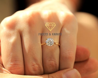 May include: A gold engagement ring with a large, round, clear diamond. The ring is on a person's finger.