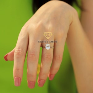 May include: A silver ring featuring an oval-cut diamond. The ring is worn on a hand with painted nails. The background is a solid green. The logo "FACETS & KARATS" is in the upper center.