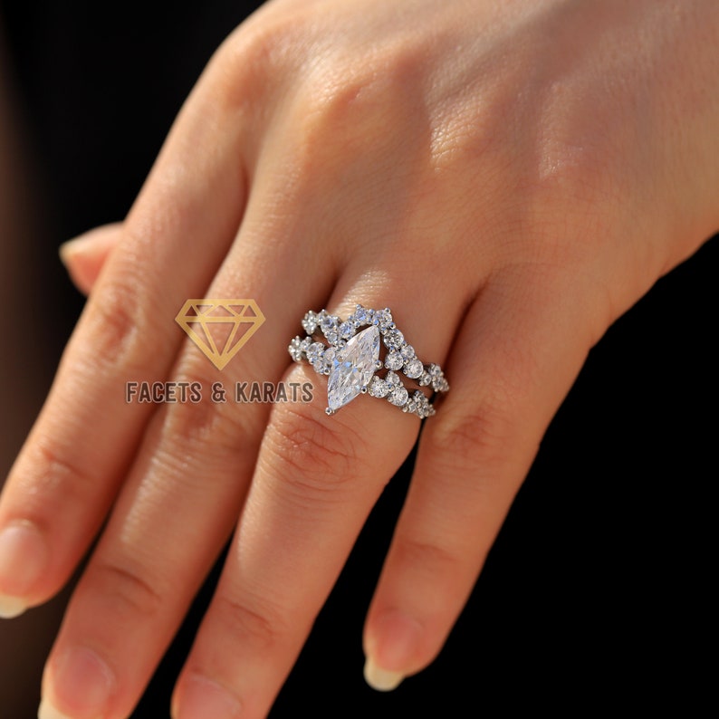May include: A silver engagement ring with a large marquise-shaped diamond surrounded by smaller diamonds. The ring has a delicate, intricate design with a double band.