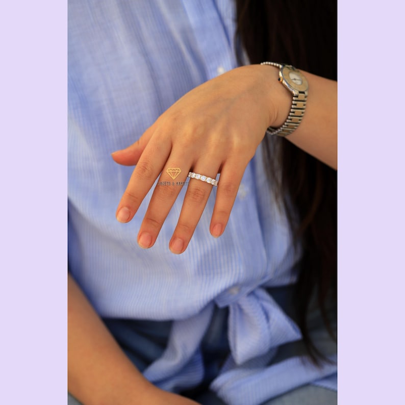 Op de afbeelding: Een zilveren ring met een rij heldere zirkonia-stenen. De ring zit aan een vinger.