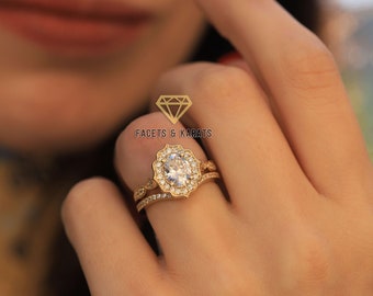 May include: A gold engagement ring set with a large oval-shaped diamond surrounded by smaller diamonds. The ring is set in a delicate floral design. The ring is worn on a person's finger.