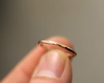 Puede incluir: Un anillo de banda de oro delgado, mostrado en un dedo.