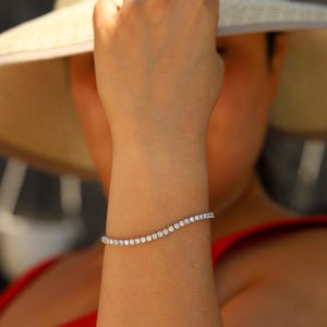 May include: A woman's wrist wearing a silver tennis bracelet with small, clear diamonds.