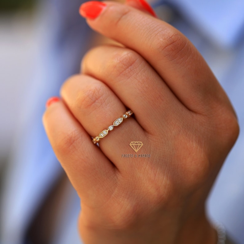 Op de afbeelding: Een delicate gouden ring met een rij kleine, ronde en ovale diamanten. De ring zit aan een vinger.