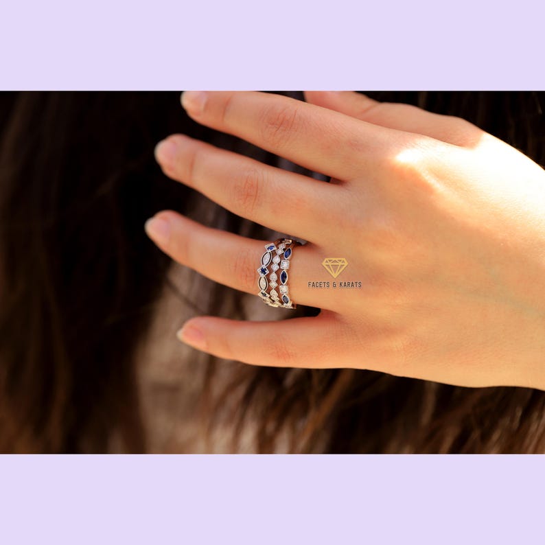 May include: Three silver rings with oval-shaped blue and white gemstones. The rings are stacked on a finger.