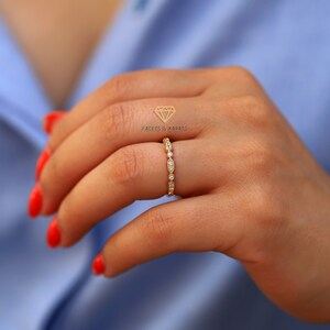 Op de afbeelding: Een delicate gouden ring met een rij kleine, ronde diamanten in een pav&eacute;-setting. De ring zit aan een vinger.