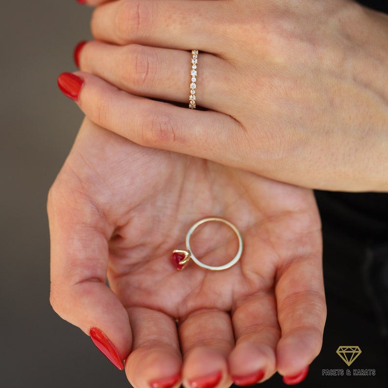 May include: Two gold rings set with gemstones. The first ring is a thin band with small round diamonds. The second ring features a single large red gemstone.