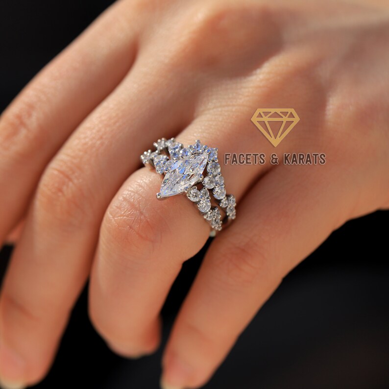 May include: A silver ring with a large marquise-shaped diamond surrounded by smaller diamonds. The ring is set on a woman's finger.