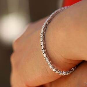 May include: A silver tennis bracelet with a row of small, clear diamonds.
