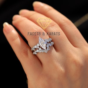 May include: A silver ring with a large marquise-shaped diamond surrounded by smaller diamonds. The ring is set on a band with a delicate, intricate design.