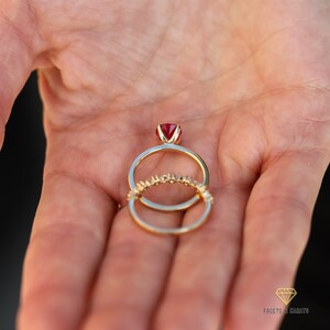 May include: A gold ring set with a red ruby gemstone, with a smaller diamond band ring worn underneath.