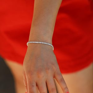 May include: A silver tennis bracelet with small round clear stones. The bracelet is on a person's wrist.