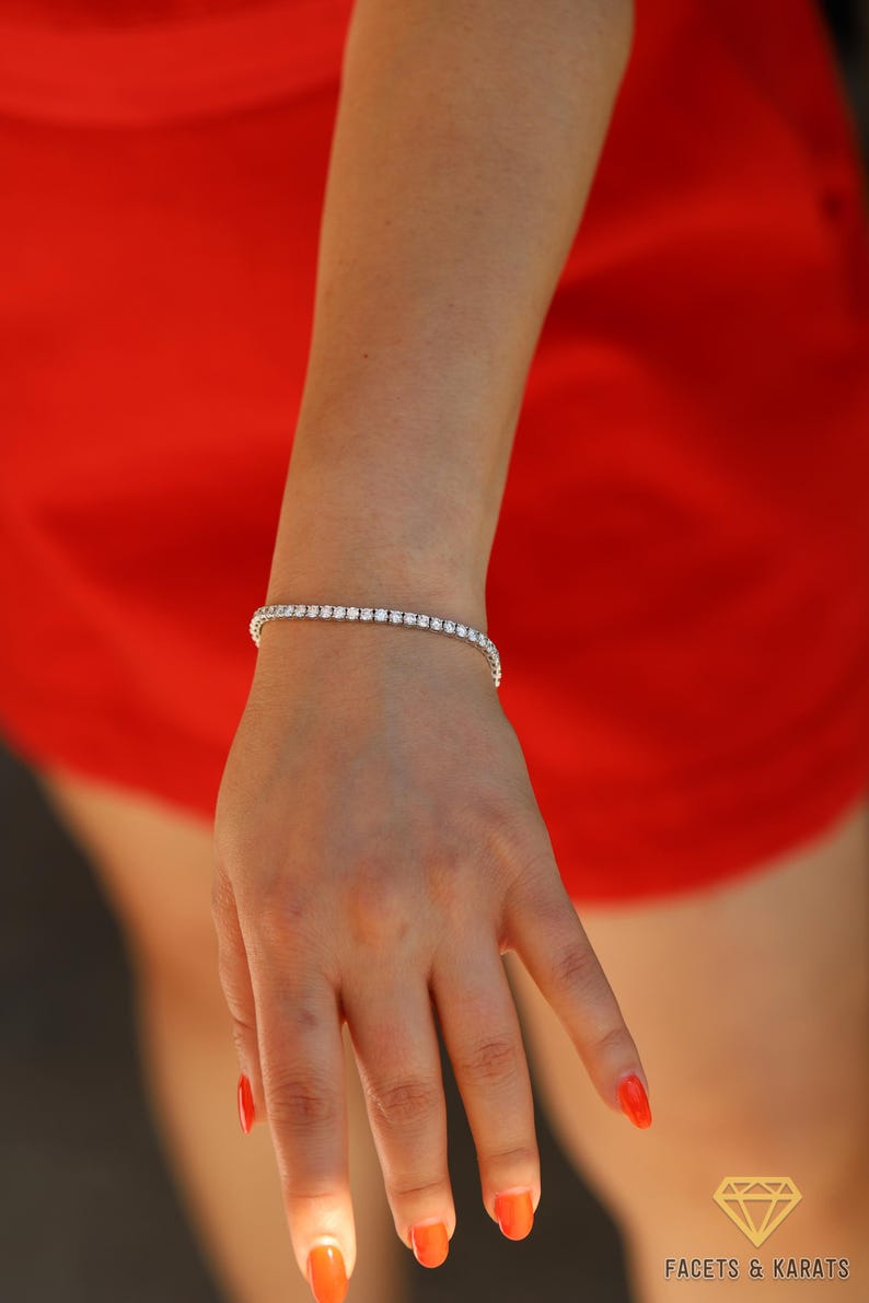 May include: A silver tennis bracelet with small round clear stones. The bracelet is on a person's wrist.