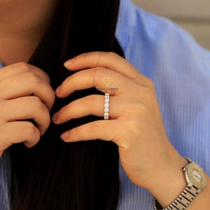 Op de afbeelding: Een gouden ring met een rij ronde, heldere edelstenen. De ring zit aan een vinger.