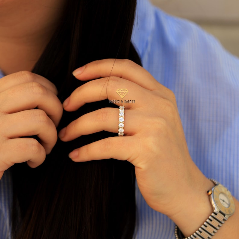 Op de afbeelding: Een gouden ring met een rij ronde, heldere edelstenen. De ring zit aan een vinger.