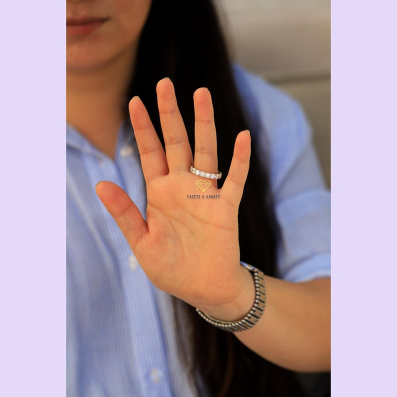 Op de afbeelding: Een close-up van een hand met een diamanten eternity band ring. De ring is gezet in een gouden band en heeft een rij kleine, ronde diamanten.