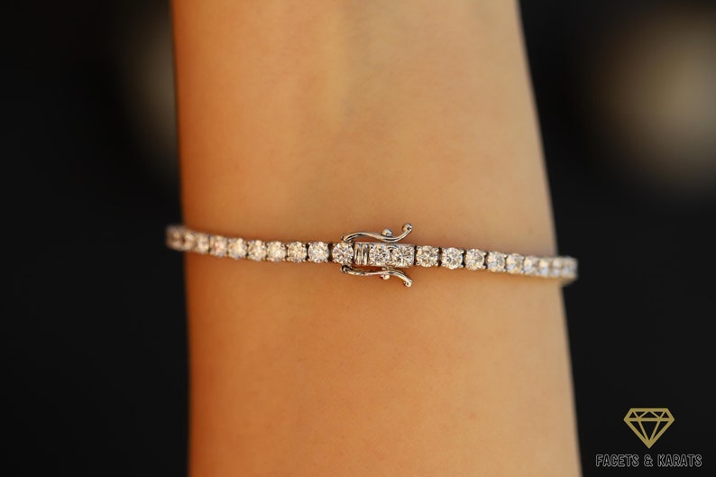 the image is showcasing the double safety clasp of a diamond tennis bracelet while being worn on the wrist. The brand name is Facets and Karats. The round cut diamonds are shining very beautifully.
