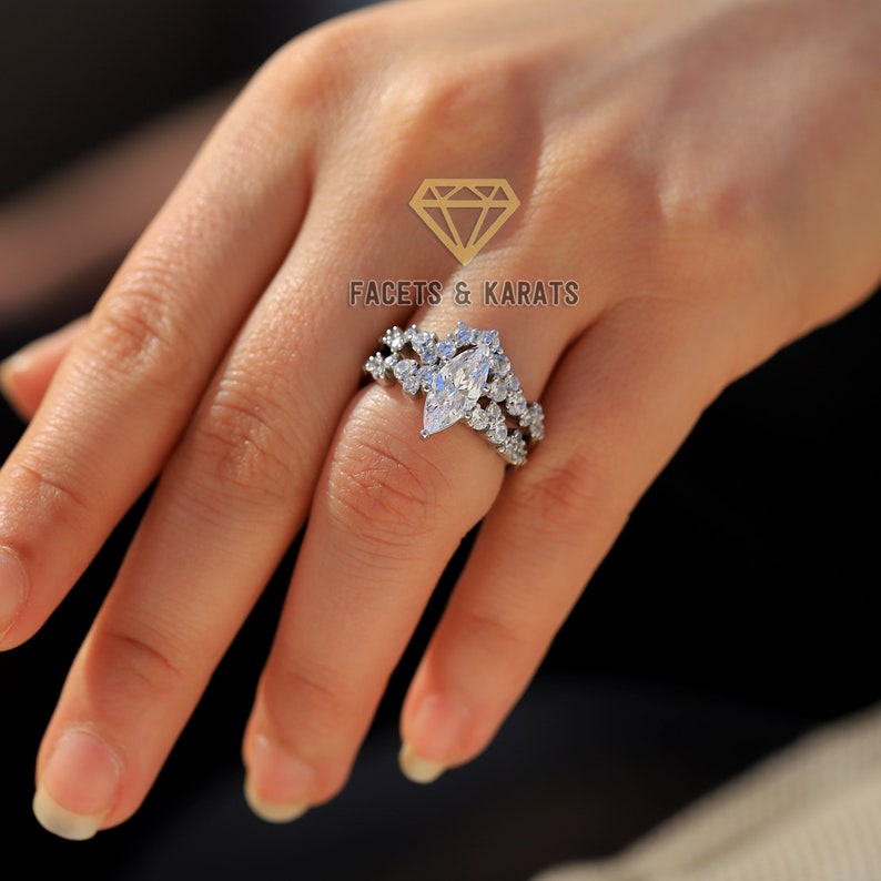 May include: A silver ring set with a large marquise-shaped diamond surrounded by smaller diamonds. The ring is worn on a person's finger.