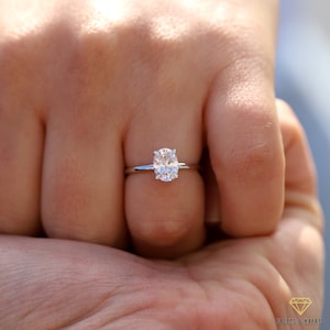 May include: A close-up of a silver engagement ring with a large oval-shaped diamond.