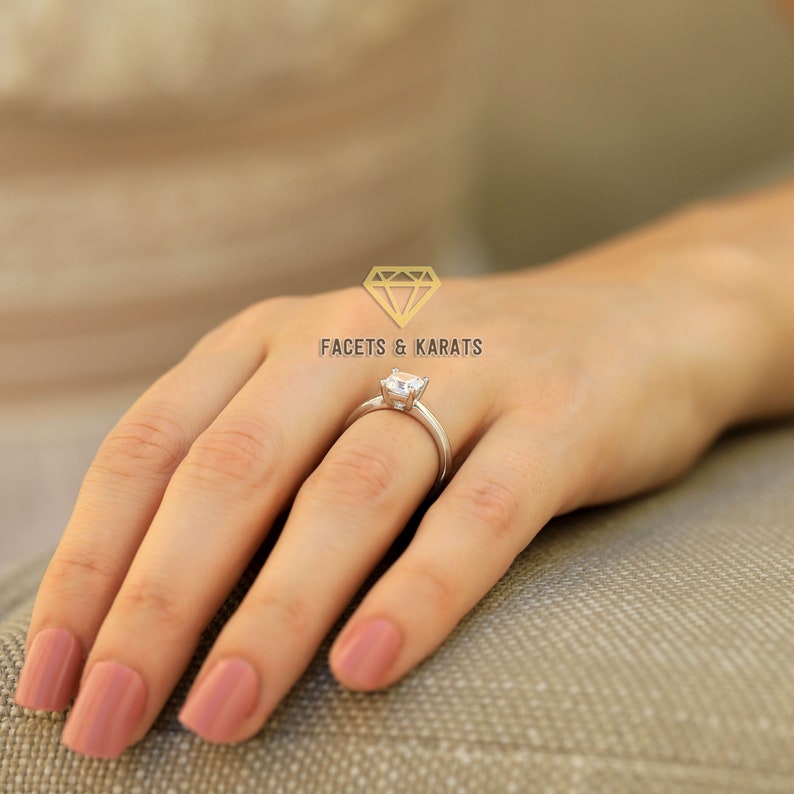 Może przedstawiać: Srebrny pierścionek z kwadratowym diamentem na palcu kobiety. Pierścionek osadzony jest na gładkiej obrączce.