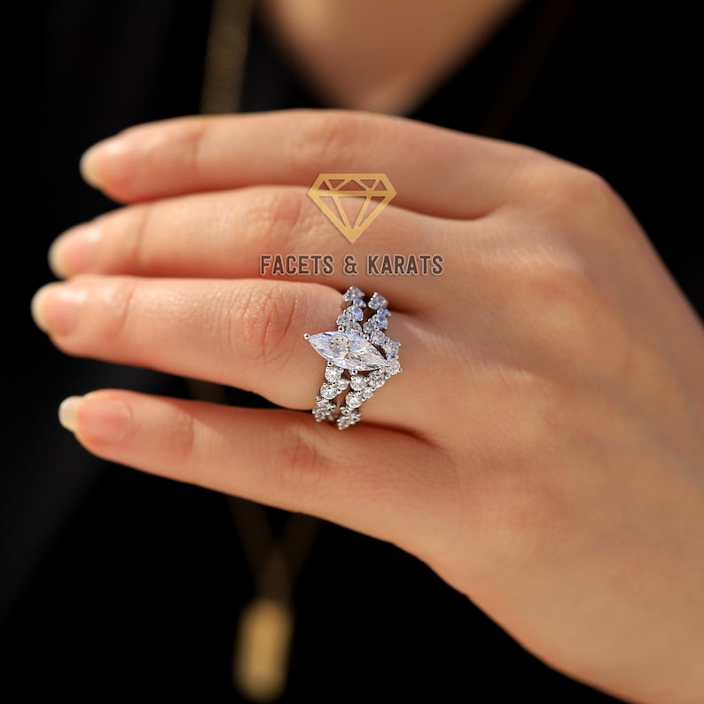 May include: A silver ring with a large marquise-shaped diamond surrounded by smaller diamonds. The ring is set on a band with a delicate, intricate design. The text "FACETS & KARATS" is visible in the background.