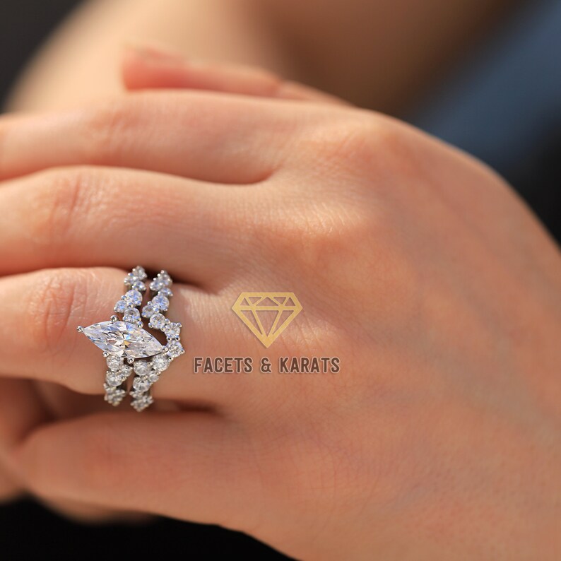 May include: A silver ring with a large marquise-shaped diamond surrounded by smaller diamonds. The ring is set on a band with a row of smaller diamonds on each side.