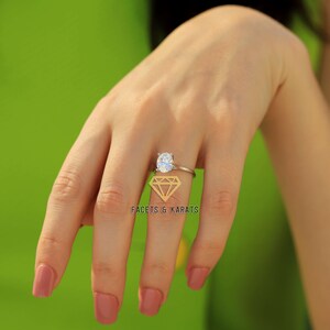 May include: A silver ring featuring an oval-cut diamond. The ring is set on a thin band and is shown on a hand with pink nail polish. The background is a solid green. The logo "FACETS & KARATS" is visible.