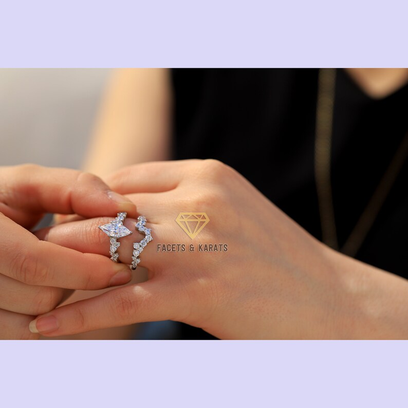 May include: A pear-shaped diamond engagement ring with a matching wedding band. The ring is set in a white metal and features a delicate, curved design. The band is adorned with small diamonds.