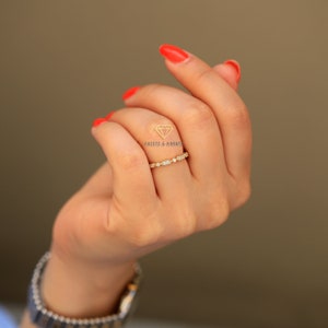 Op de afbeelding: Een delicate gouden ring met een rij kleine ronde en ovale diamanten. De ring zit aan een vinger.