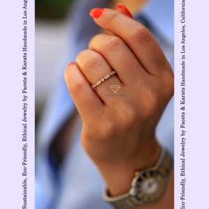 Op de afbeelding: Een delicate gouden ring met een rij kleine, ronde diamanten in pav&eacute;-zetting. De ring zit aan een vinger.