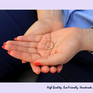 Op de afbeelding: Een gouden ring met kleine diamanten gezet in een delicate band. De ring wordt in de palm van een hand gehouden.