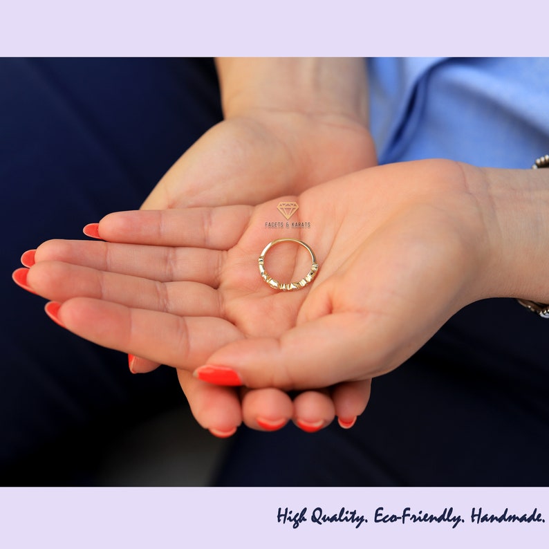 Op de afbeelding: Een gouden ring met kleine diamanten gezet in een delicate band. De ring wordt in de palm van een hand gehouden.