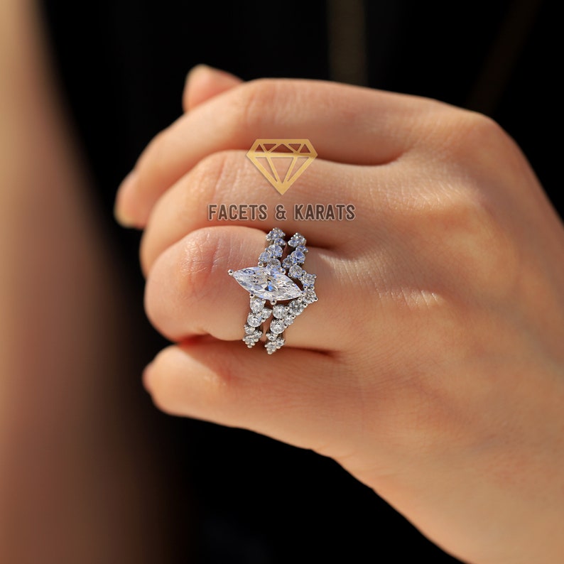 May include: A silver ring with a large marquise-shaped diamond and smaller diamonds set in a delicate band. The ring is worn on the finger of a hand.