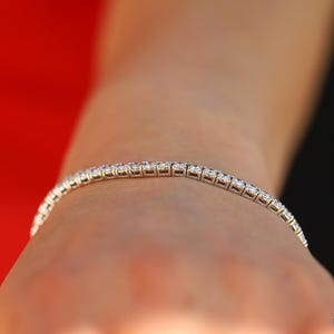 May include: A silver tennis bracelet with small round diamonds set in a continuous line.