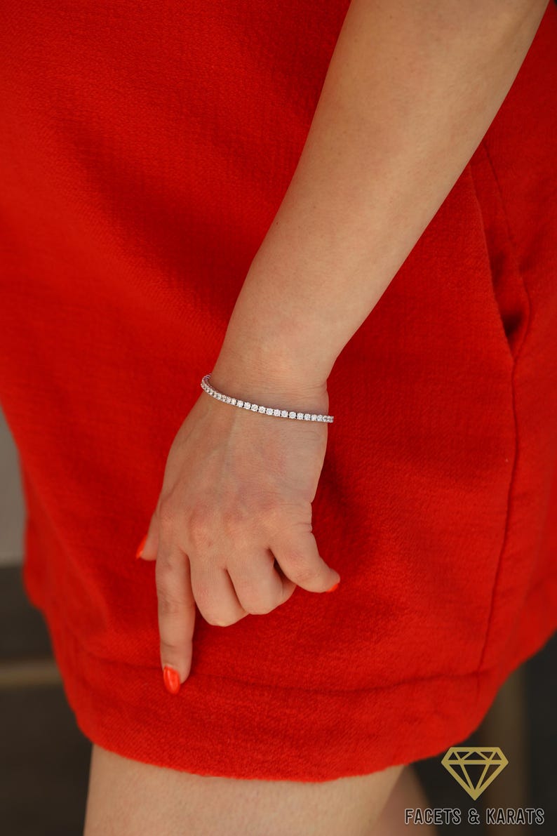 May include: A silver tennis bracelet with small, clear cubic zirconia stones. The bracelet is on a woman's wrist.