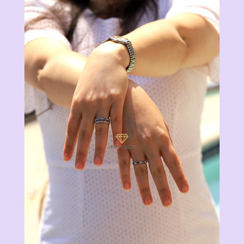 May include: Two silver rings with small black stones set in a circle. The rings are worn on the fingers of a person's hand.