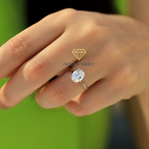 May include: A silver engagement ring featuring an oval-cut diamond. The ring is set on a slender band and is shown on a hand. The text "FACETS & KARATS" is visible.