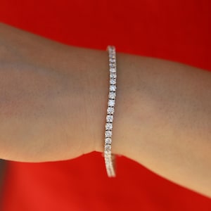 May include: A silver tennis bracelet with a row of clear round stones.