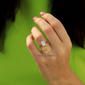 May include: A silver ring with a large, oval-cut diamond is shown on a hand. The ring's band is slender, and the diamond is the focal point. The background is a bright green, with the text "FACETS & KARATS" and a diamond logo.
