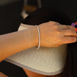May include: A silver tennis bracelet with small round diamonds set in a continuous line.